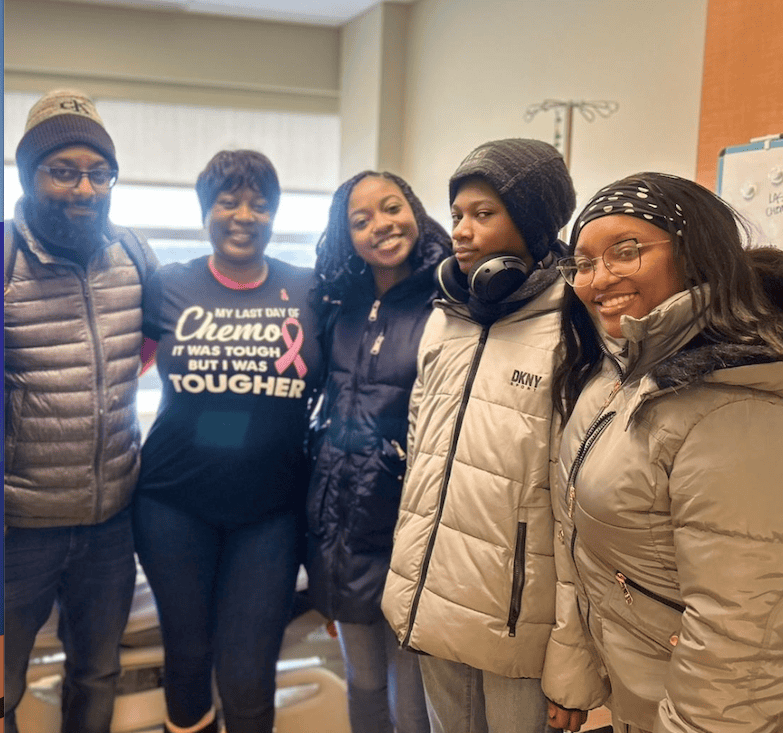 Shanise and her husband stand with their son and daughters, smiling at the camera. Shanise wears a shirt celebrating her last day of chemo.